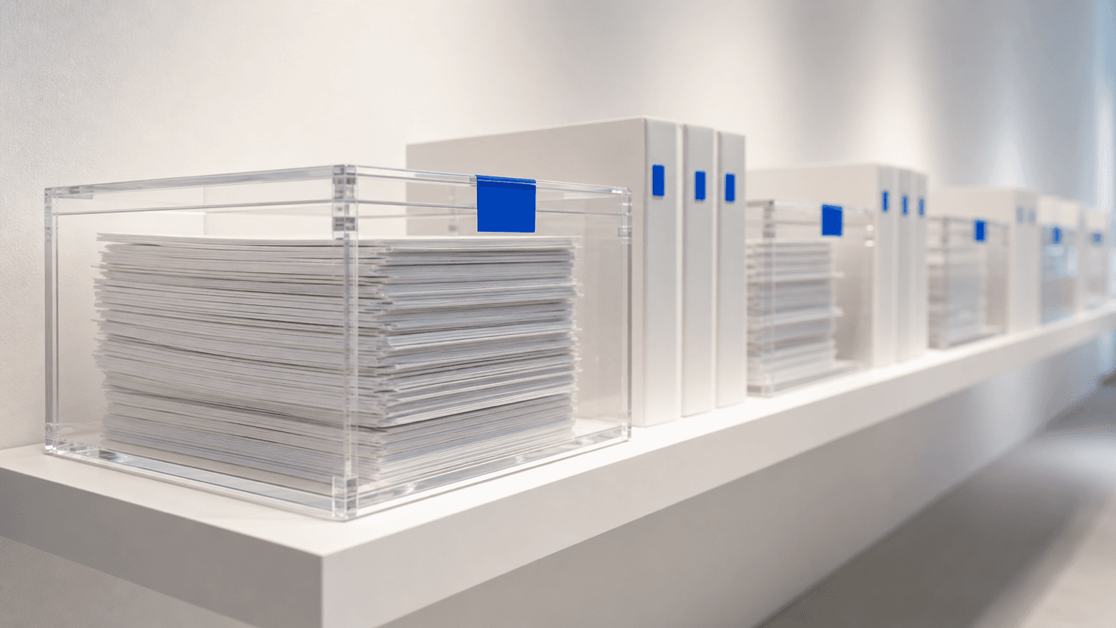 Sealed acrylic archive boxes and binders with cobalt index tabs on a floating gallery shelf