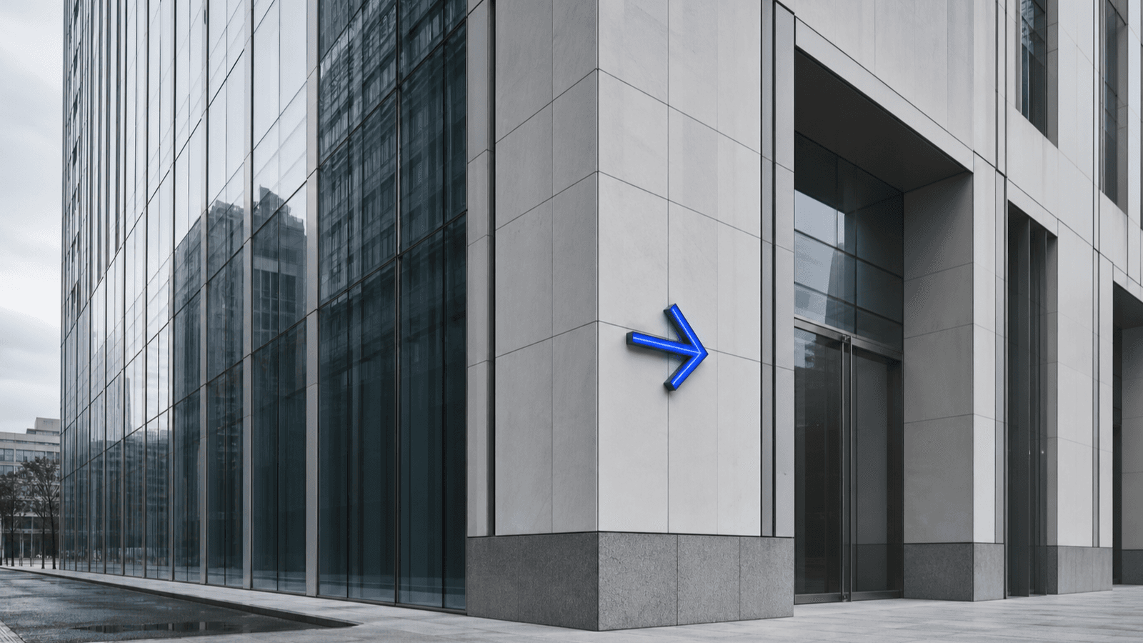 A steel-and-glass building corner at street level with a single cobalt-lit directional wayfinding arrow mounted on the facade