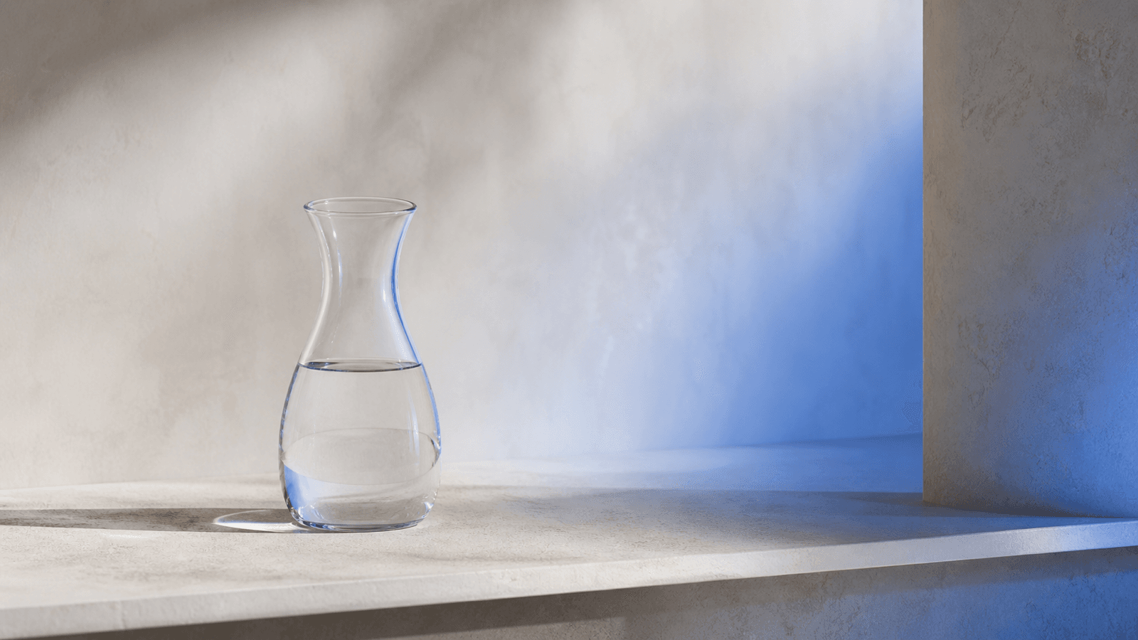 A glass water carafe lit by an ambient cobalt glow from an unseen source
